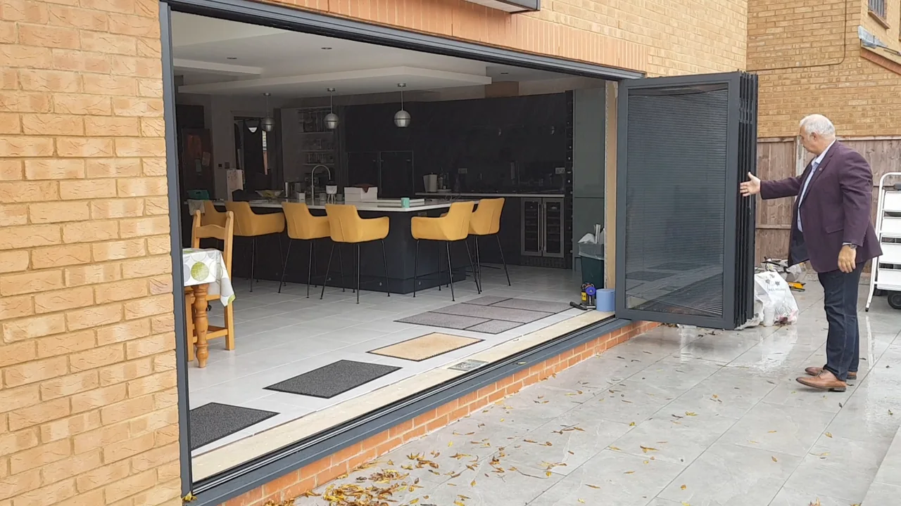 OpenGlide-deuren in houtskoolkleur die uitkomen op een keuken met gele barkrukken
